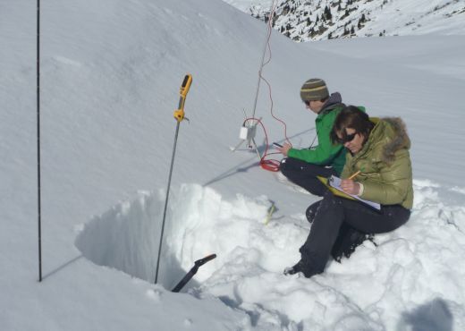 Photo of two research staff members conducting a field test in deep snow, performing various measurement routines to determine snow hardness.