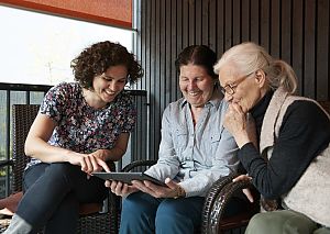 Three women in front of a tablet, with one explaining digital support options for home care.